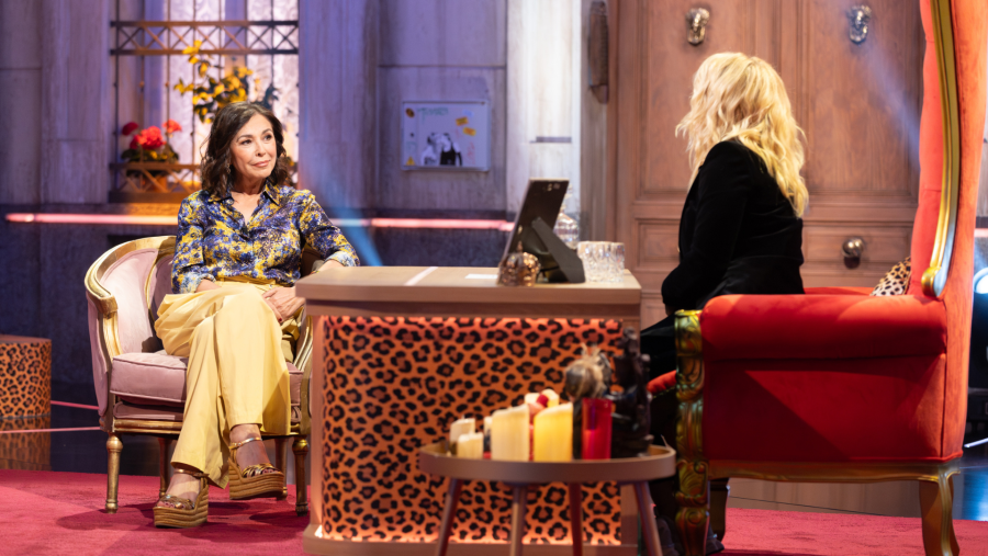 Isabel Gemio y Henar Álvarez en un plató de televisión, sentadas en sillones decorados, con una mesa central con estampado de leopardo.