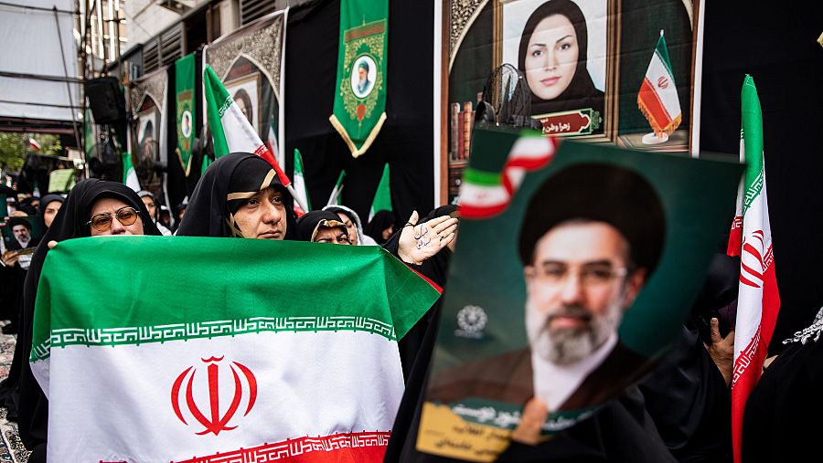 Mujeres con hiyabs negros en Irán participan en una congregación pública, una de ellas ondea la bandera iraní con 