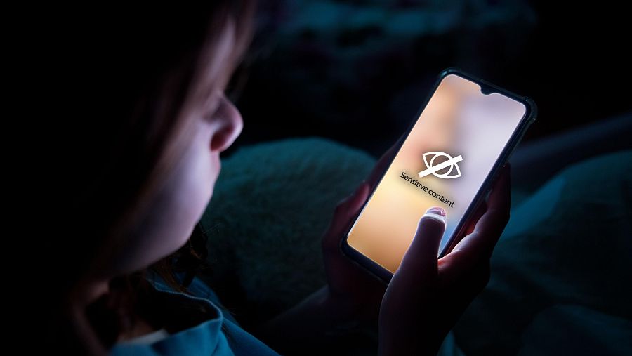 Un menor viendo a oscuras la pantalla de un móvil donde puede leerse la frase en inglés 