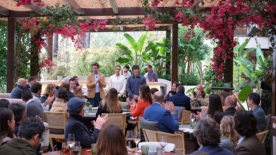 Jueces de MasterChef España, Jordi Cruz, Samantha Vallejo-Nágera y Pepe Rodríguez, en una presentación al aire libre bajo buganvillas, interactuando con una audiencia aplaudiendo.