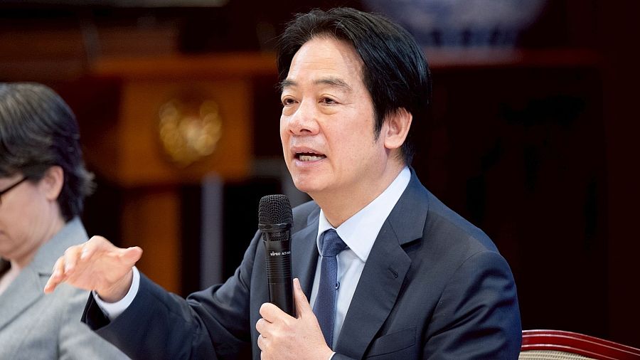 Primer plano del presidente de Taiwán, Lai Ching-te, en una rueda de prensa, hablando con un micrófono y gesticulando con la mano derecha. Expresión seria y concentrada.