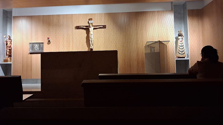 En la penumbra de la capilla de la T4 rezan dos mujeres y un joven.