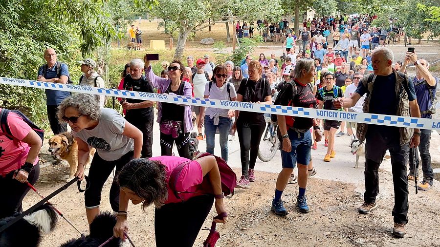 Participants de la caminada creuen per sota de la línia policial que barra el pas al camí de Can Catà