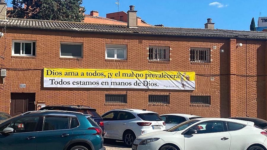 Pancarta en la fachada de la antigua parroquia de Santa Bibiana, en Villaverde Alto, con una frase de León XIV sobre los colores del Vaticano.