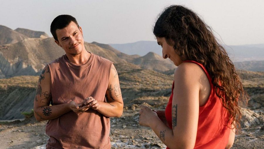 Iván Hadoum, actor español, posa en un paisaje desértico con una mujer a su lado. Ambos lucen tatuajes y vestimenta informal.