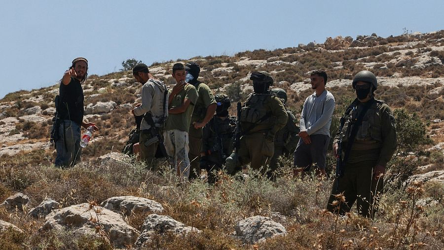 Militares israelíes armados y civiles en un paisaje rocoso de Cisjordania.