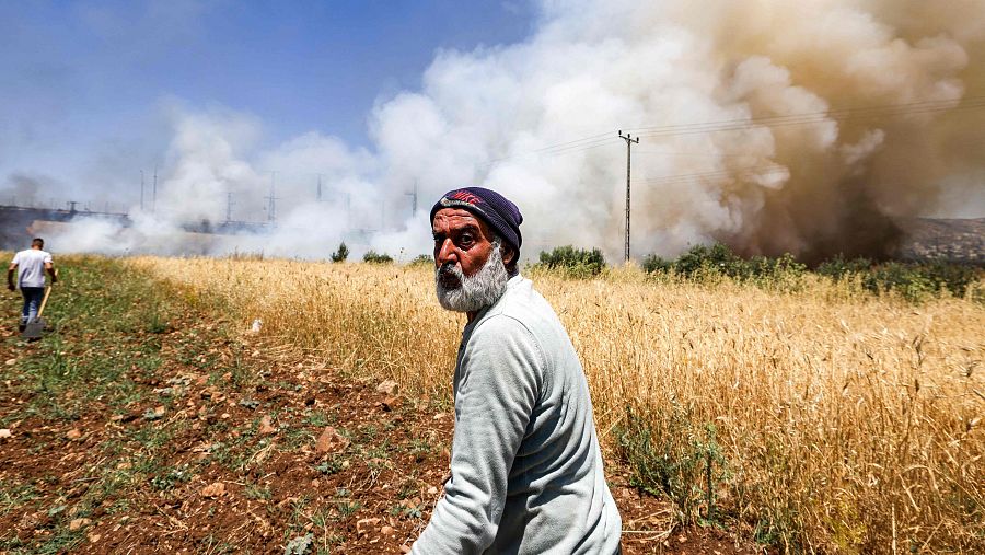 Hombres intentan apagar un incendio en un campo agrícola en Huwara, Cisjordania, bajo un cielo con humo. Un hombre mayor observa, otro se dirige al fuego con una pala.