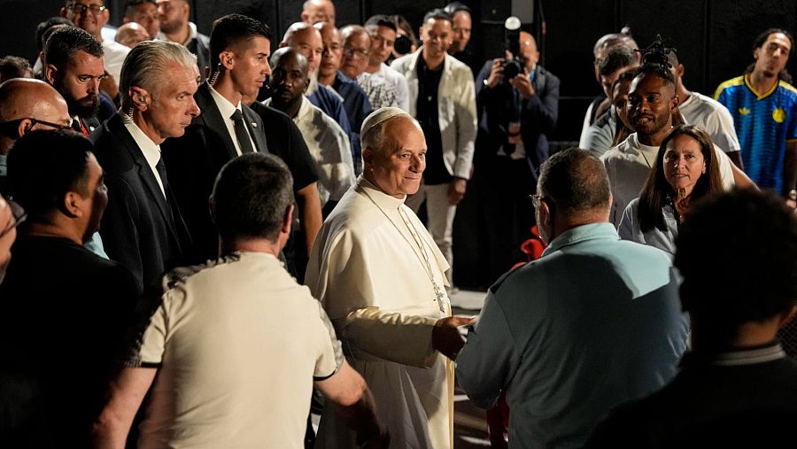 El Papa Francisco interactúa con presos y personal en la prisión de Brians 1, vestido de blanco, rodeado de una multitud diversa y medios de comunicación.