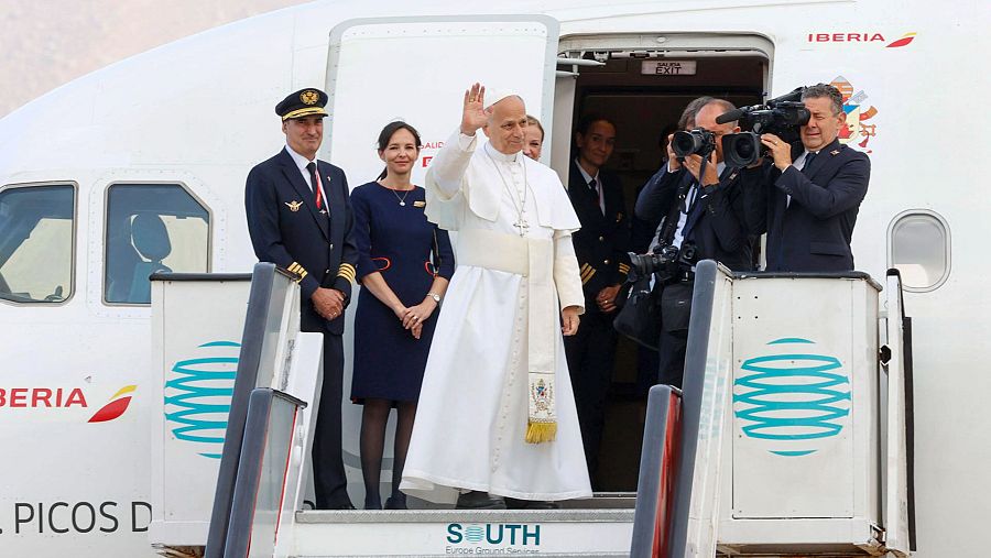 El Papa Francisco saluda desde la escalinata de un avión de Iberia, acompañado por personal de cabina y pilotos, mientras cámaras registran su despedida en un aeropuerto.