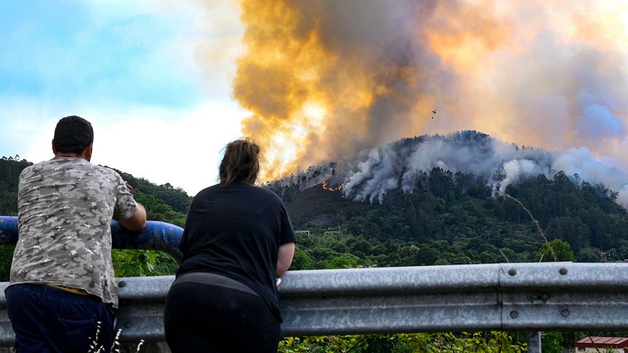 Dos vecinos de la localidad asturiana de Peñaflor (Grado), observan el incendo forestal declarado este sábado.