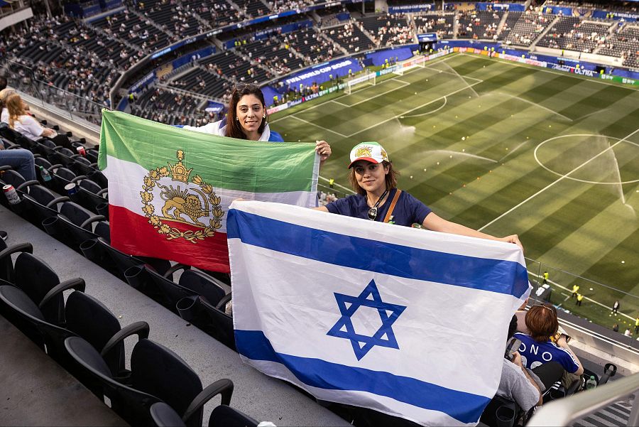 Aficionadas muestran una bandera iraní prerrevolucionaria y una bandera israelí antes del partido entre Irán y Nueva Zelanda