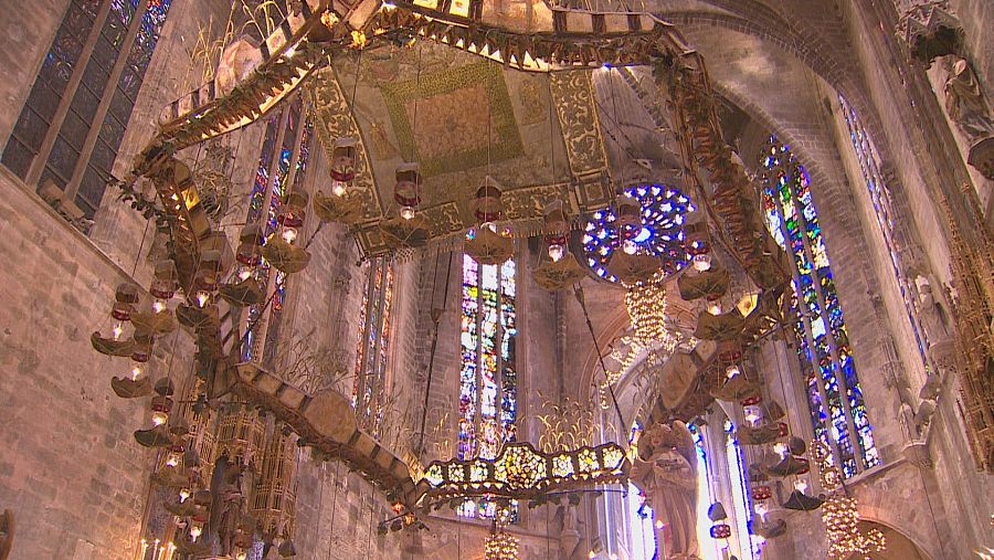 Interior de la Catedral de Palma de Mallorca, con el baldaquino de Gaudí y vidrieras de colores. Vista desde un ángulo bajo que resalta la grandiosidad arquitectónica.