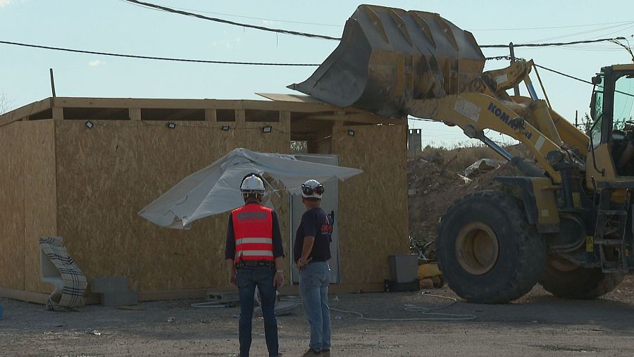 Hombres con cascos blancos y chaleco reflectante observan cargadora KOMATSU amarilla con cucharón elevado sobre estructura de madera en obra.