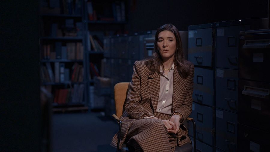 Gabriela Echeverría, bisnieta de Antonio Ortega, posa sentada con traje de cuadros en un archivo. Su mirada es directa y serena.