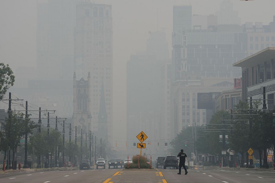 Un peatón cruza la calle mientras el perfil urbano de Detroit queda oculto por la mala calidad del aire debido al humo de los incendios forestales canadienses