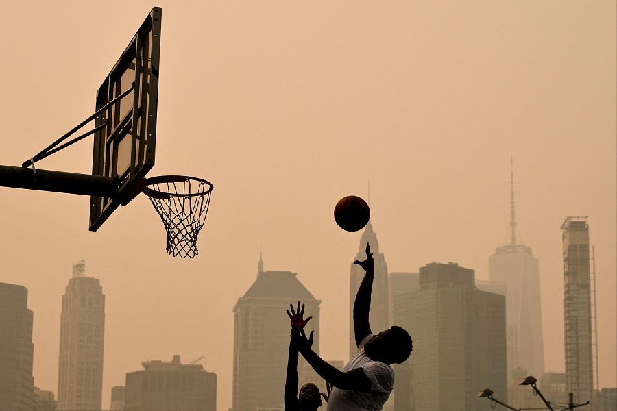 Varias personas juegan al baloncesto mientras el humo de los incendios forestales procedentes de Canadá provoca condiciones de neblina en Nueva York