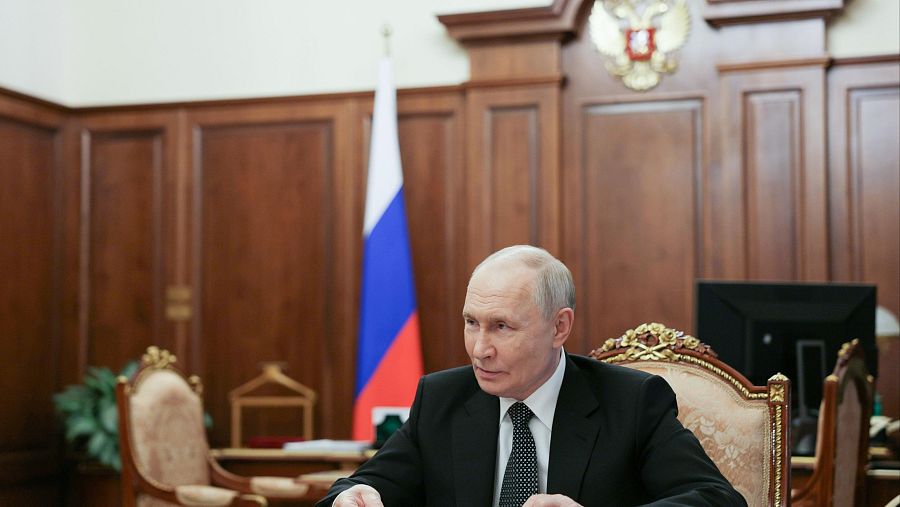 Retrato de Vladímir Putin en un despacho oficial, con traje oscuro y corbata. Detrás, la bandera rusa y el escudo de armas.