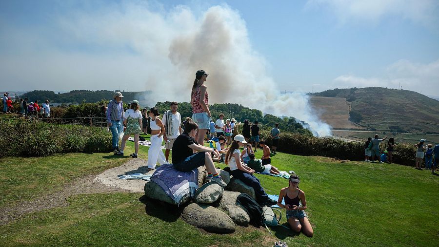 Varias personas observan un incendio forestal cerca del lugar donde se reunirán para presenciar el eclipse