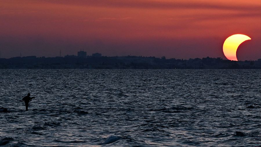 Un hombre pesca mientras observa el eclipse solar parcial en la playa de Soliman, en la provincia de Nabeul, Túnez