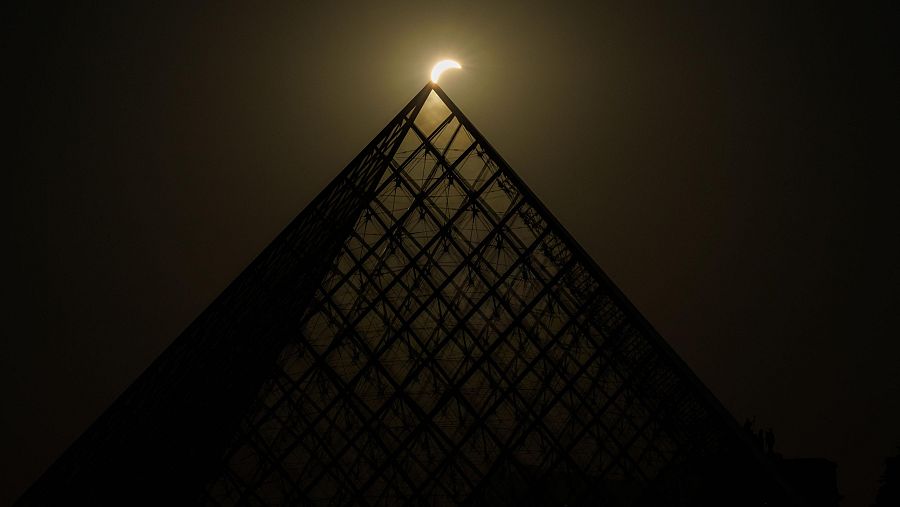 La luna pasa por encima del horizonte del sol detrás de la Pirámide del Louvre, en París