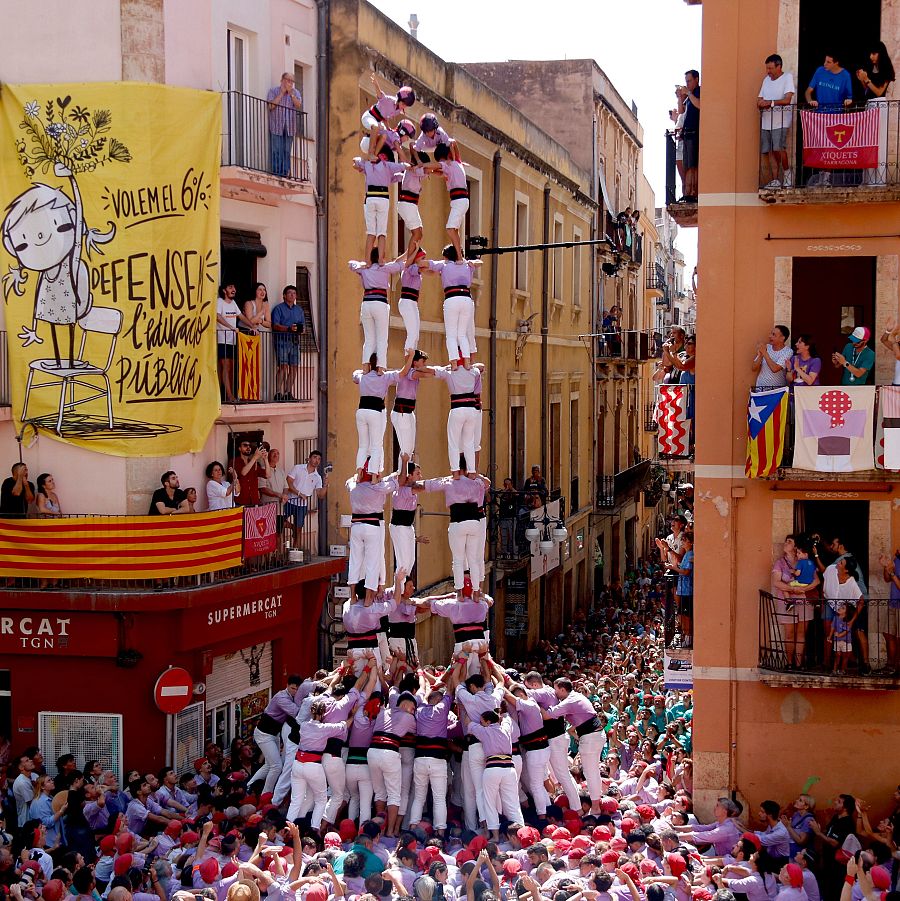 Torre humana de 8-9 niveles en calle con multitud. 