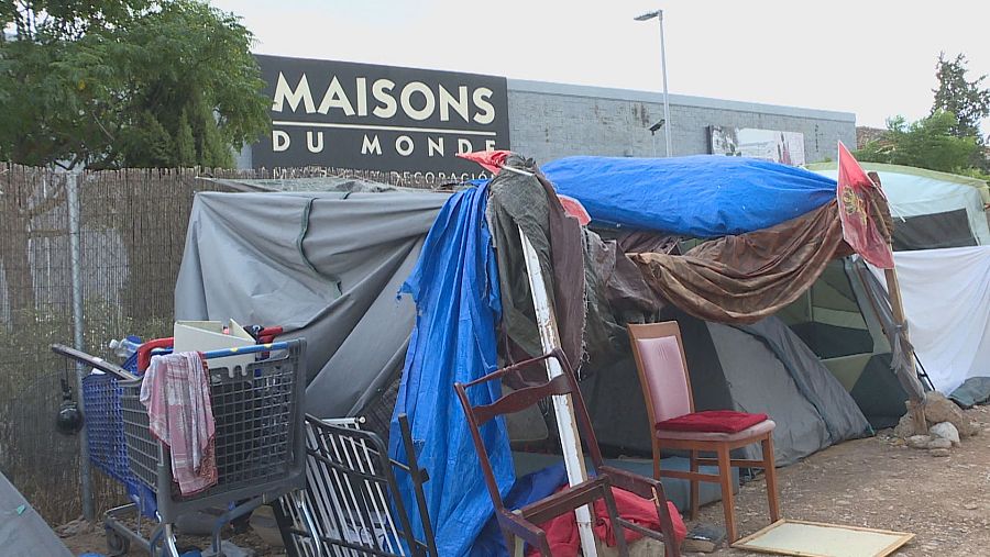 Asentamiento improvisado con tiendas y lonas azules, frente a un edificio de 