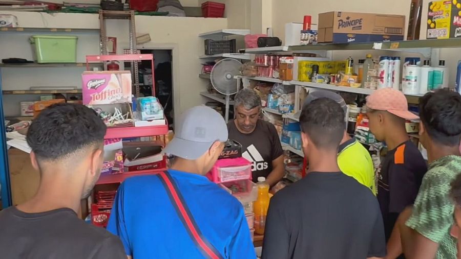 Lahsen, comerciante de ultramarinos, atiende a jóvenes clientes en su tienda repleta de productos, destacando 