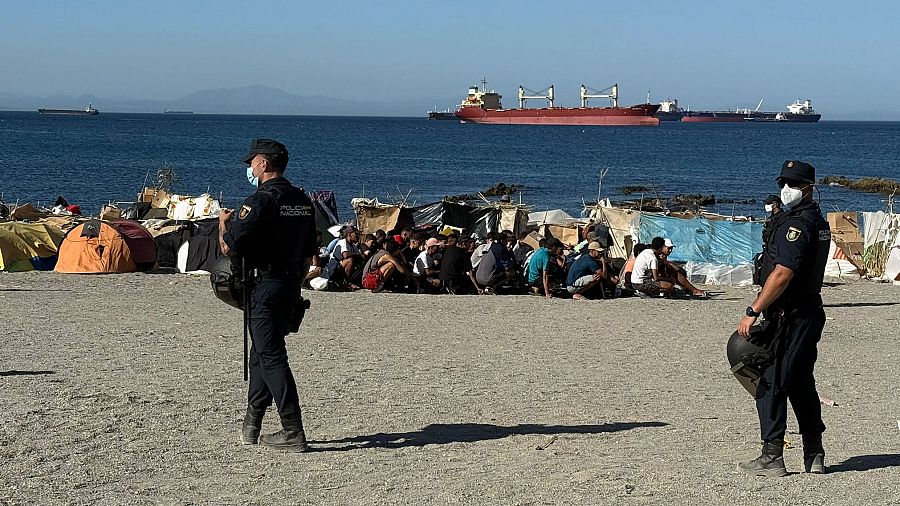 Agentes de la Policía Nacional en la Playa del Trampolín de Ceuta, junto a un campamento de migrantes y el mar Mediterráneo al fondo.