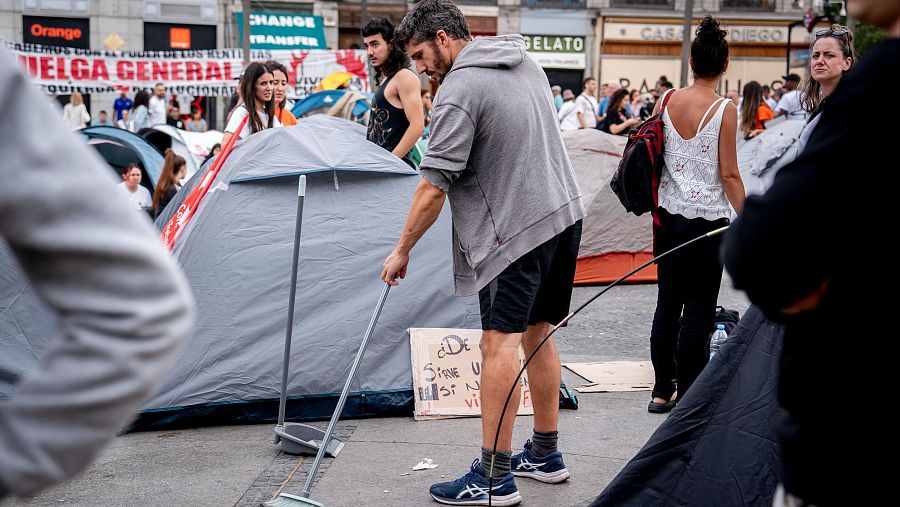 Una persona con un cepillo recoge la suciedad en la zona de tiendas de campaña en Sol