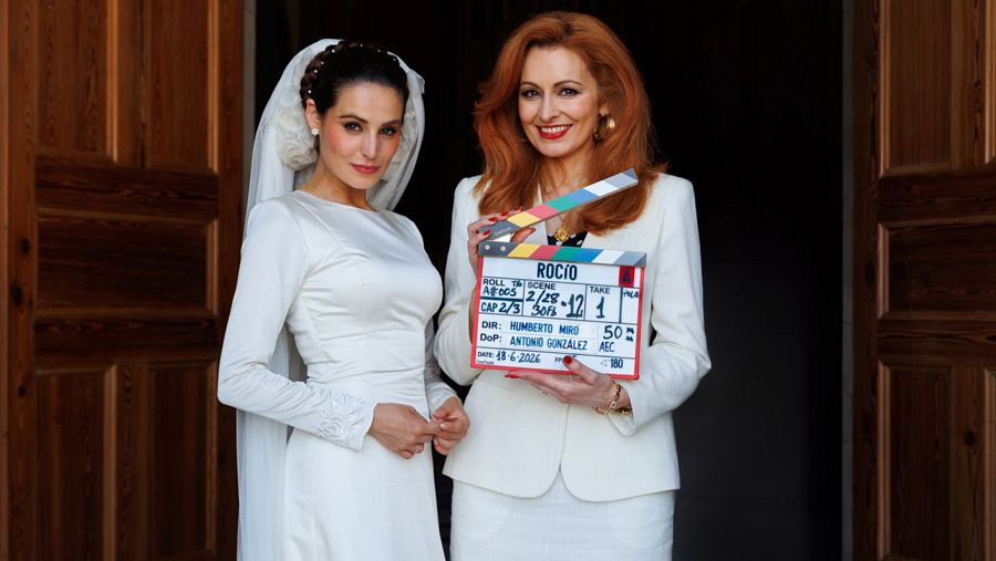 Carmen Fernández Raigón y Susana Córdoba, vestidas de blanco, posan con una claqueta que indica 