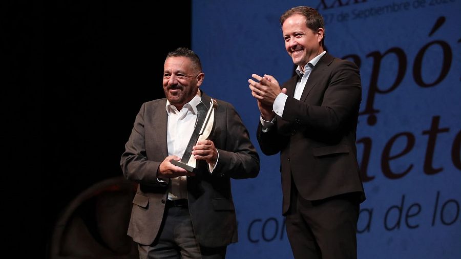 Pepón Nieto recibe un trofeo plateado, mientras Carlos Velázquez aplaude. La pantalla de fondo indica 