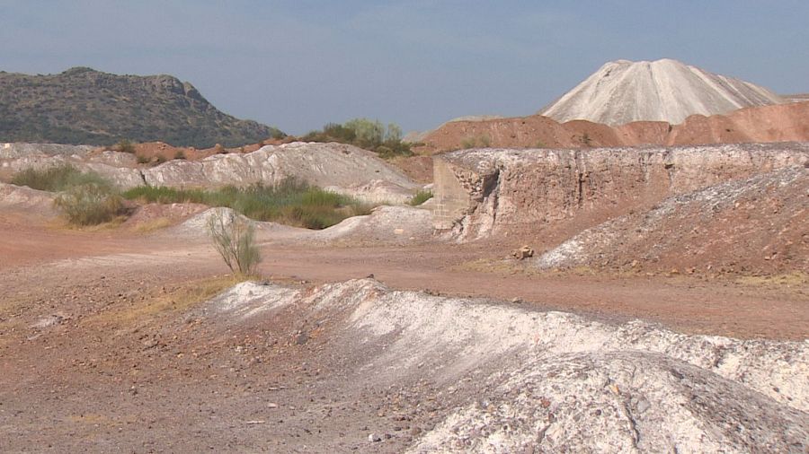 Paisaje de las Minas de Tierrablanca en La Zarza, Extremadura, con montículos de arcilla blanca, una gran escombrera cónica al fondo y vegetación dispersa bajo un cielo despejado.