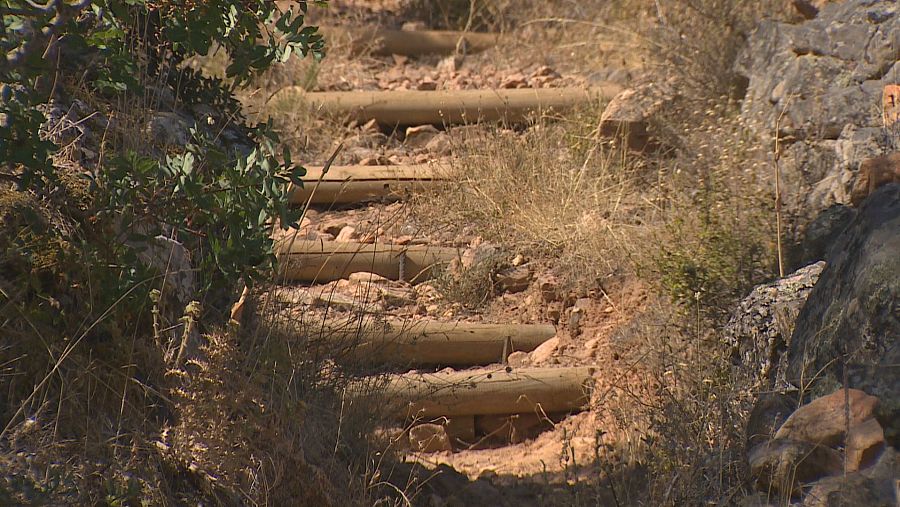 Sendero empinado con escalones de troncos de madera en la bajada de las Hoyas de la Ruta Peñas Blancas en La Zarza, Extremadura, rodeado de vegetación seca y rocas.