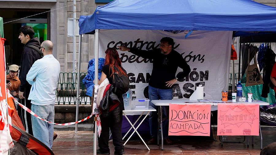 Punto de información con una mesa y carteles de donación en una acampada reivindicativa al aire libre.