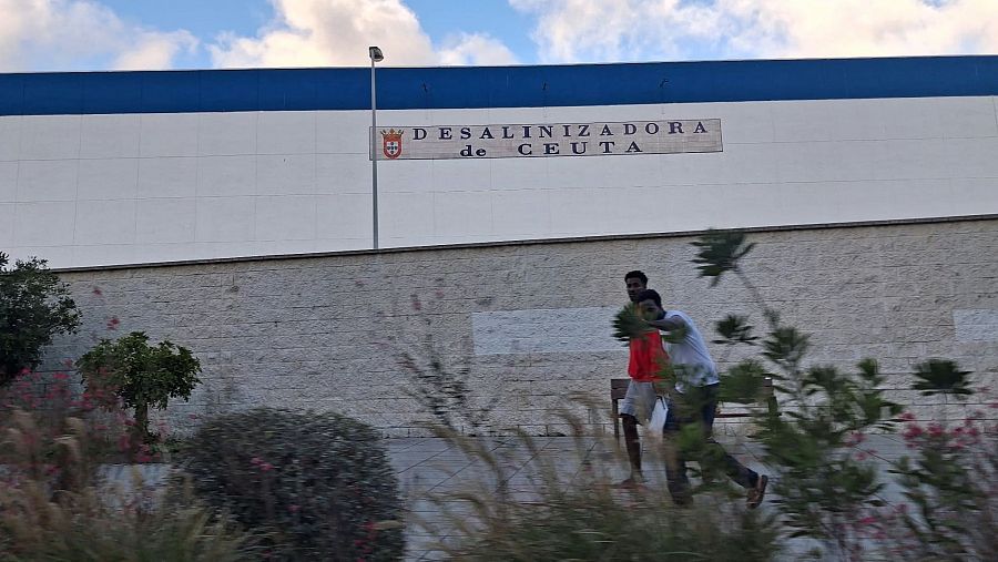 Dos inmigrantes subsaharianos saludan al paso por la desalinizadora de Ceuta.