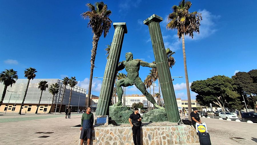 Inmigrantes por los alrededores de la estatua de Hércules en el puerto de Ceuta