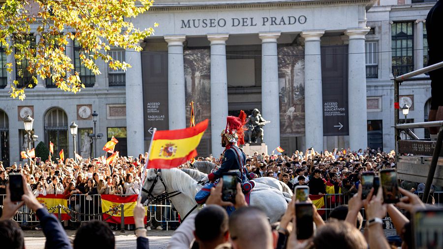 Varias personas disfrutan del desfile durante el acto solemne de homenaje a la bandera nacional y desfile militar por el 12 de octubre, Día de la Hispanidad, en la Plaza de Cánovas del Castillo, a 12 de octubre de 2026, en Madrid (España).