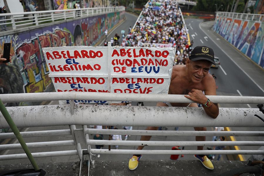 Un hombre se cuelga de un paso elevado peatonal en Cali sosteniendo un cartel que critica al presidente colombiano Abelardo de la Espriella