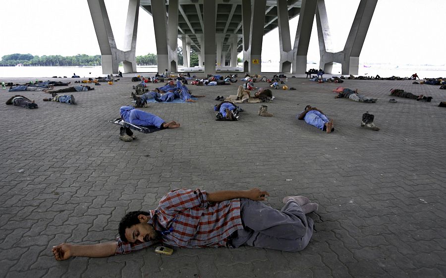 Trabajadores de la construcción duermen bajo un puente durante el decanso para comer en Singapur.