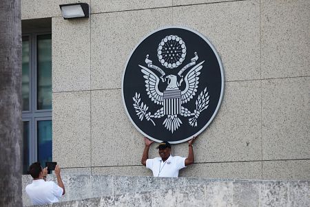 Dos agentes de seguridad se fotografían con el escudo de los Estados Unidos sobre el muro de la embajada de Washington en La Habana.