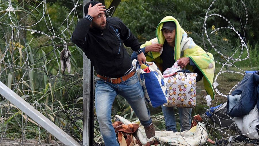 Refugiados cruzan a través de un agujero en la alambrada que separa Serbia de Hungría cerca de Roszke, en este último país. AFP PHOTO / ATTILA KISBENEDEK