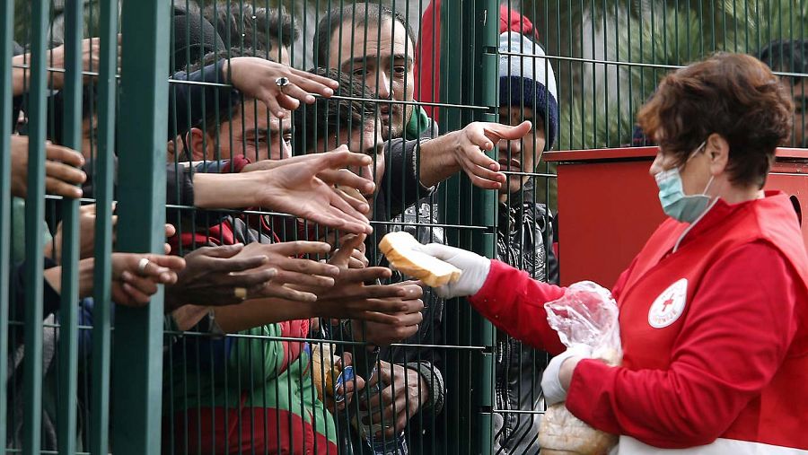 Una trabajadora de la Cruz Roja ofrece pan a los refugiados tras una valla en el campo de refugiados en Brezice (Eslovenia) hoy, 21 de octubre de 2015. EFE/Antonio Bat