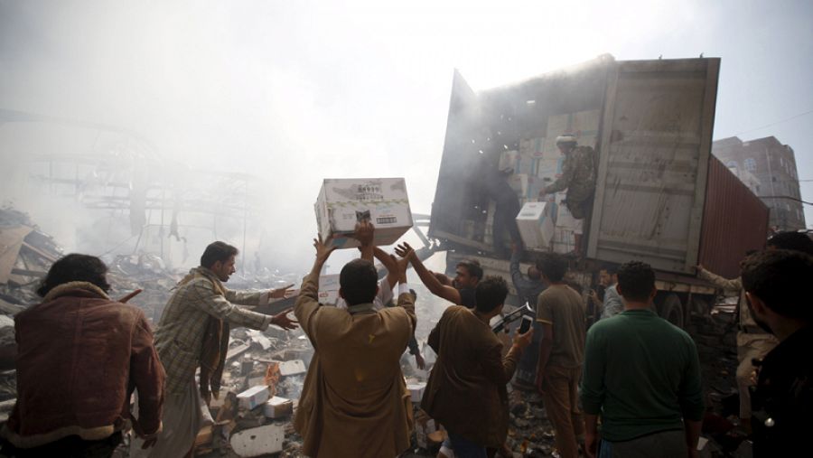 Yemeníes rescatando cajas con víveres tras un bombardeo saudí a un banco de alimentos en Saná