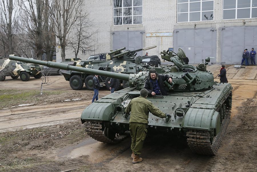 Varios trabajadores conversan junto a los tanques que esperan para ser reparados en una fábrica de vehículos blindados en Kiev