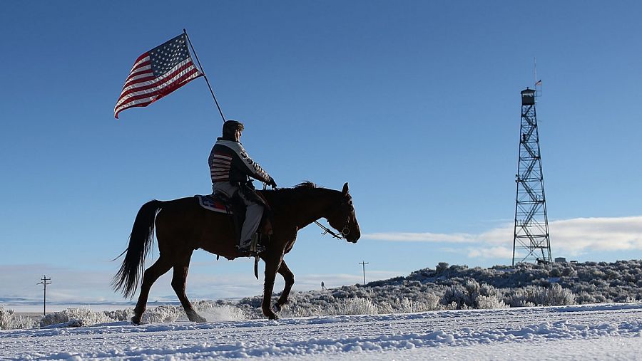 El miliciano Duane Ehmer sostiene una bandera estadounidense sobre su caballo Hellboy