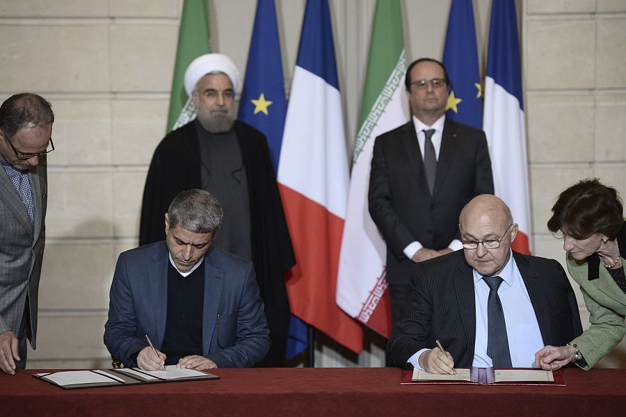 El ministro francés de Finanzas, Michel Sapin (a la derecha) y su homólogo iraní, Alí Tayebnia (a la izquierda), firman algunos de los acuerdos bilaterales en presencia del presidente iraní, Hasán Rohaní, y el presidente francés, François Hollande