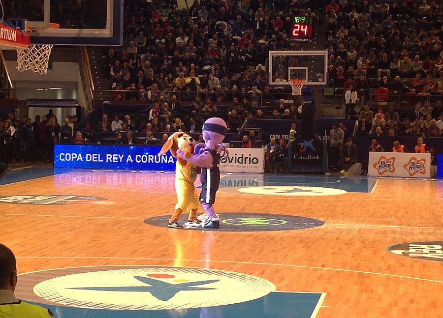 La mascota del Obradoiro baila con la mascota del Herbalife en medio de la pista.