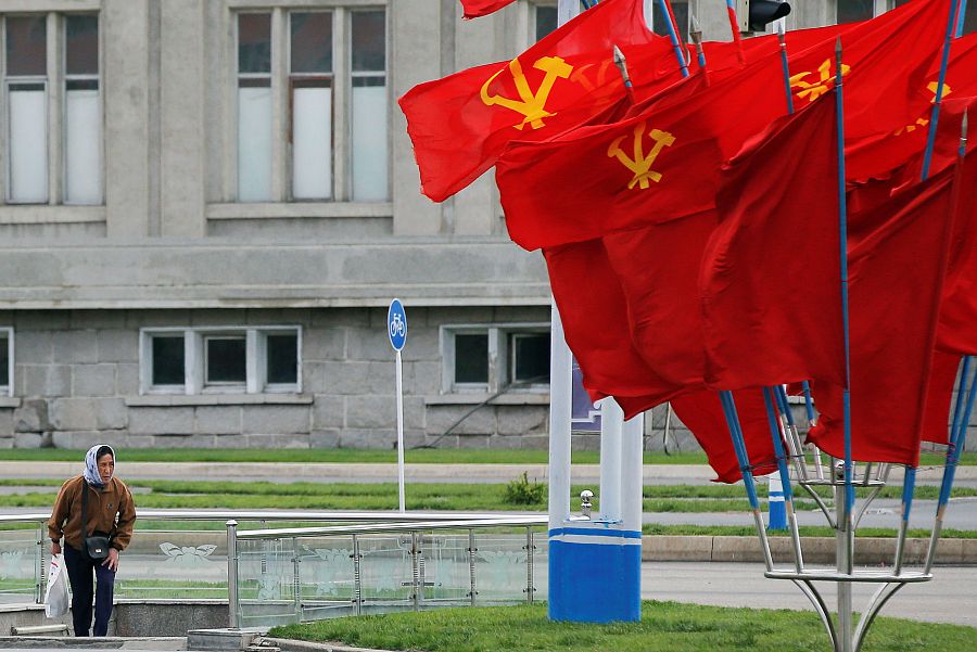 Una mujer pasa cerca de varias banderas con el emblema del Partido de los Trabajadores de Corea del Norte