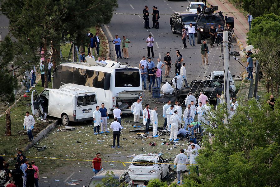 Los expertos forenses examinan el lugar donde ha explotado el coche bomba en Diyarbakir, al paso de un vehículo de la policía