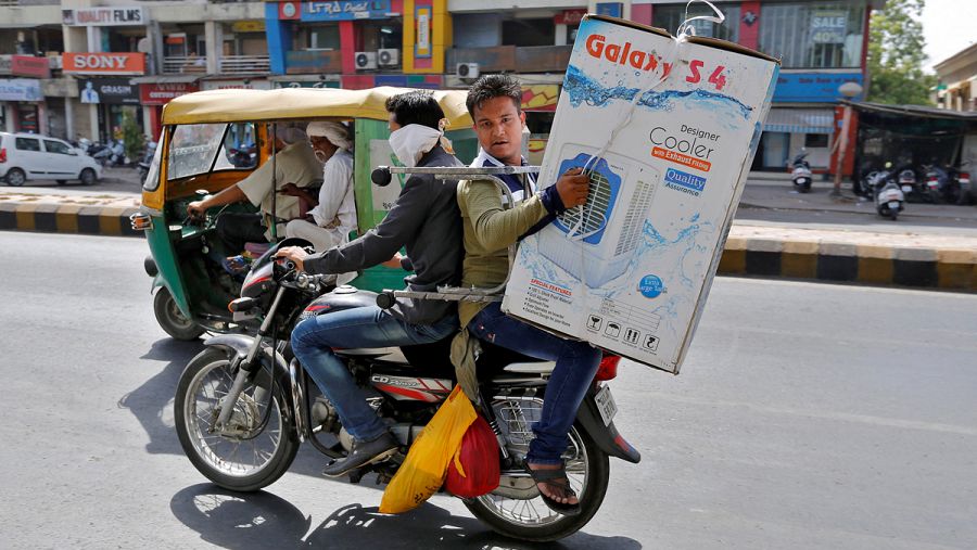 Un hombre en moto carga un aparato de aire acondicionado en Ahmedabad